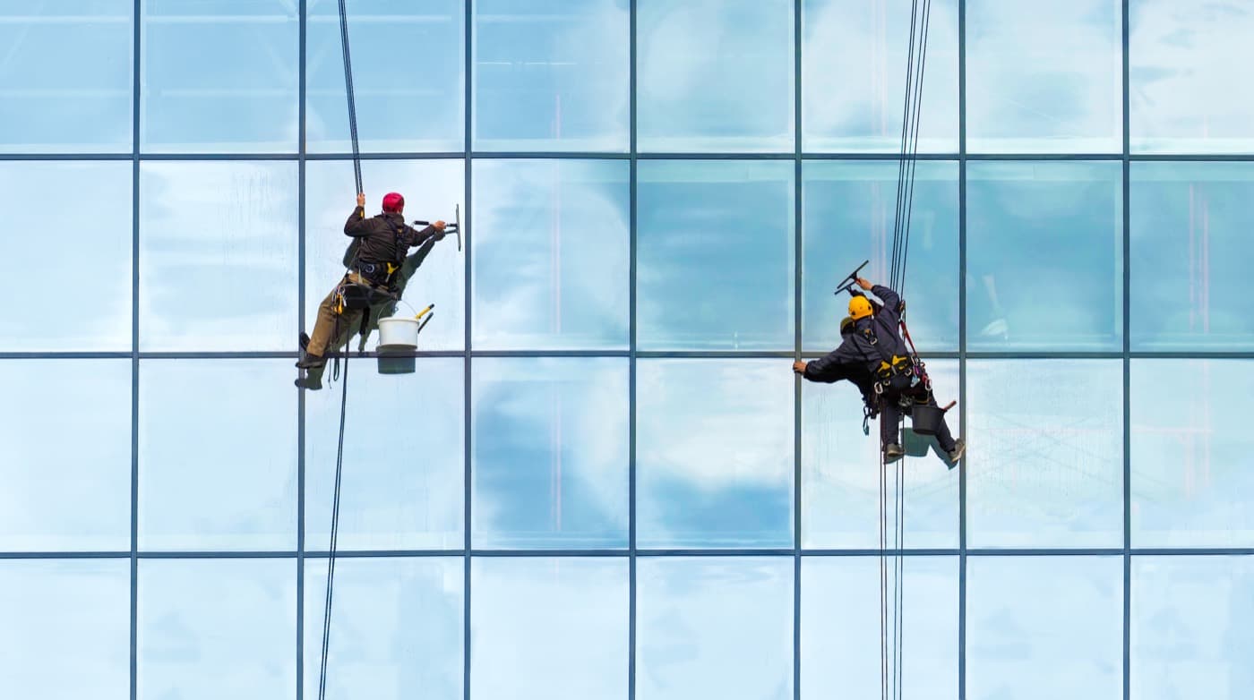 Two professional window cleaners suspended on a commercial glass building